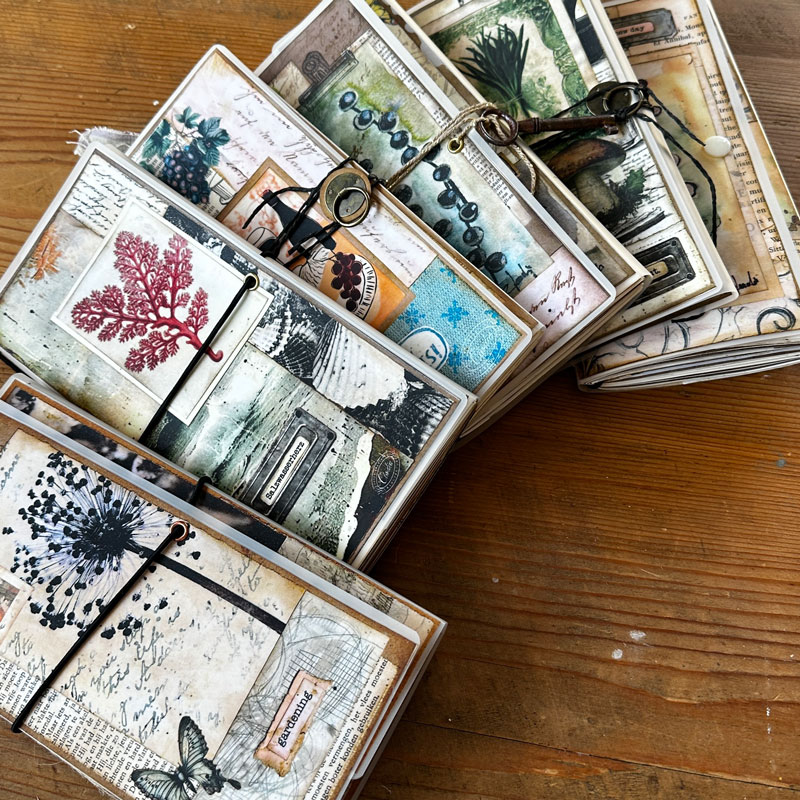 Journals mit Papierarbeiten und Naturmotiven auf einem Holztisch